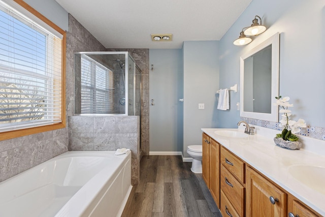 bathroom with wood finished floors, double vanity, a sink, a shower stall, and a bath