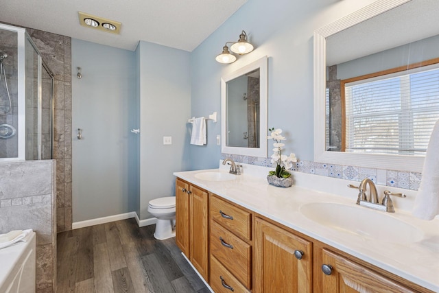 bathroom featuring wood finished floors, toilet, tiled shower, and a sink