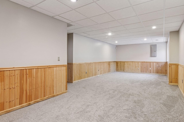 carpeted empty room with electric panel, a drop ceiling, recessed lighting, wooden walls, and wainscoting