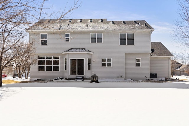 snow covered house with central air condition unit, roof with shingles, and entry steps