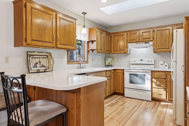 kitchen featuring under cabinet range hood, a peninsula, white appliances, a skylight, and a sink