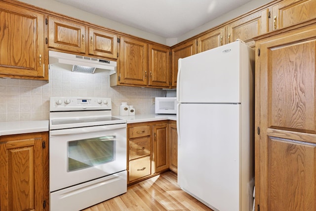 kitchen featuring white appliances, light wood finished floors, light countertops, under cabinet range hood, and backsplash