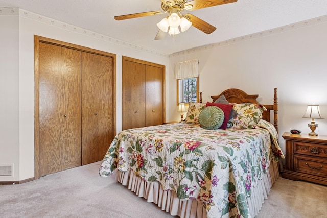 carpeted bedroom with a ceiling fan, visible vents, and two closets