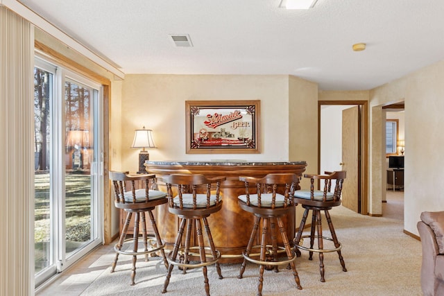 carpeted dining area featuring a bar, a textured ceiling, visible vents, and a wealth of natural light