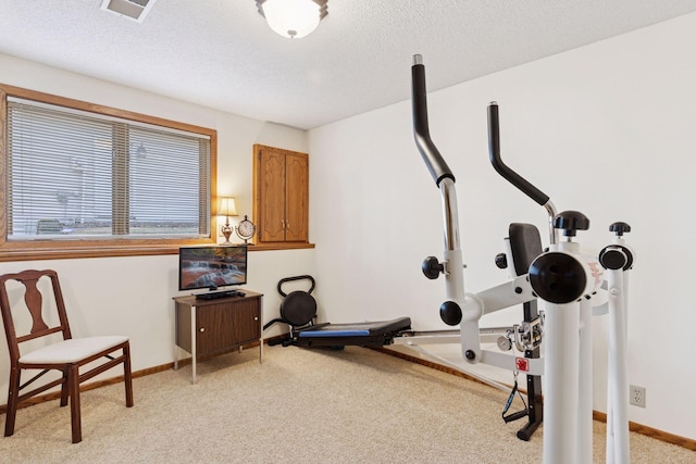 exercise area with visible vents, baseboards, a textured ceiling, and light colored carpet