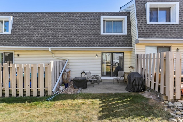 rear view of house featuring mansard roof, a patio, roof with shingles, fence, and a yard