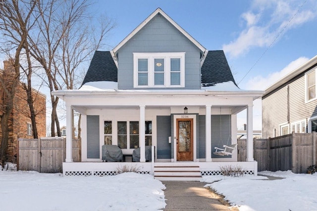 view of front of house with a shingled roof, covered porch, and fence