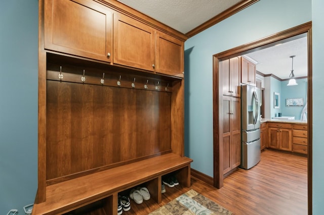 mudroom featuring a textured ceiling, ornamental molding, wood finished floors, and baseboards