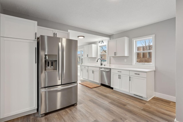 kitchen with light countertops, light wood-style flooring, appliances with stainless steel finishes, white cabinetry, and a sink