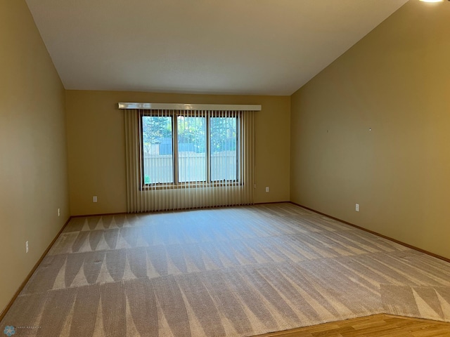 carpeted empty room featuring baseboards and vaulted ceiling