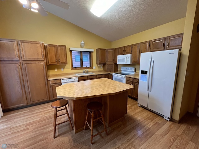 kitchen featuring a center island, a breakfast bar, lofted ceiling, white appliances, and a sink