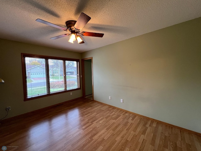 spare room featuring baseboards, a textured ceiling, light wood-type flooring, and a ceiling fan