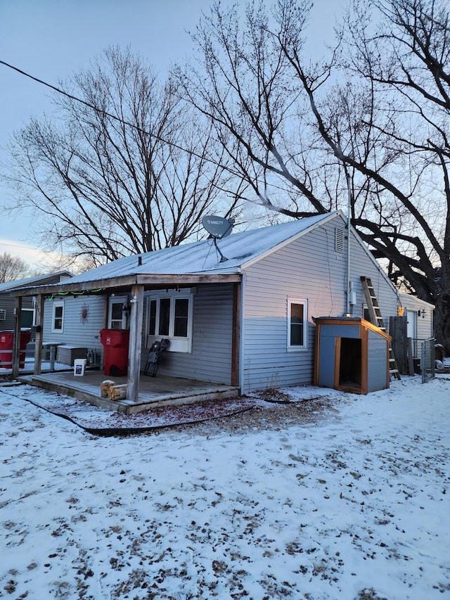 snow covered back of property featuring a shed and an outdoor structure