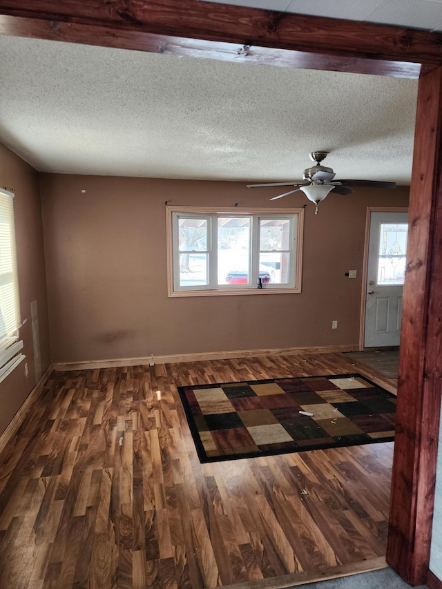 unfurnished room featuring ceiling fan, a textured ceiling, baseboards, and dark wood-type flooring