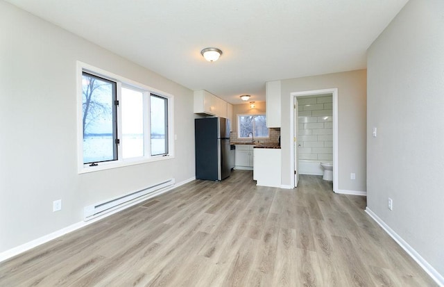 unfurnished living room with light wood-style floors, a baseboard radiator, baseboards, and a sink