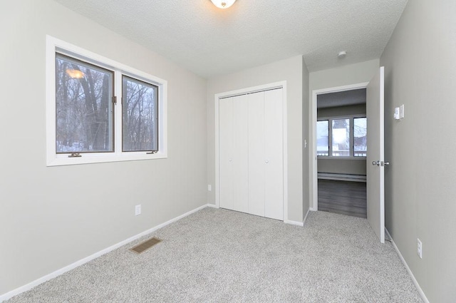 unfurnished bedroom with a textured ceiling, light colored carpet, a baseboard heating unit, visible vents, and a closet