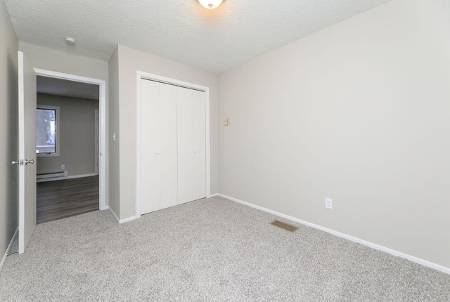 unfurnished bedroom with a textured ceiling, carpet floors, baseboards, a closet, and baseboard heating