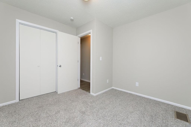 unfurnished bedroom featuring a closet, light colored carpet, visible vents, a textured ceiling, and baseboards