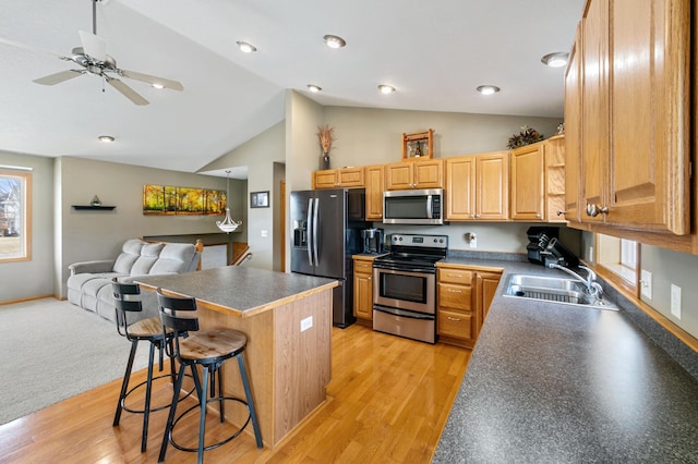 kitchen featuring dark countertops, open floor plan, a breakfast bar area, stainless steel appliances, and a sink