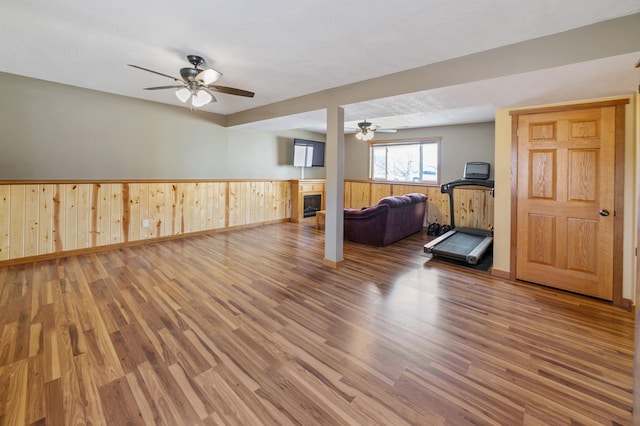 workout room featuring ceiling fan, a wainscoted wall, wood finished floors, and a glass covered fireplace