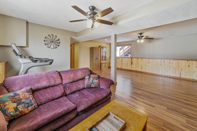 living area featuring a wainscoted wall, a textured ceiling, wood finished floors, and a ceiling fan