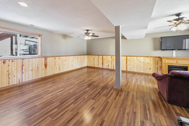 living room featuring a wainscoted wall, a textured ceiling, a ceiling fan, and wood finished floors