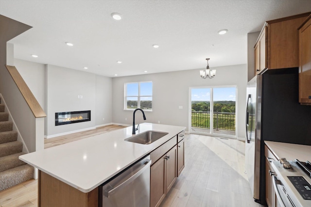 kitchen featuring a kitchen island with sink, stainless steel appliances, a sink, open floor plan, and light countertops