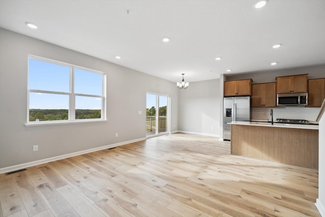 kitchen with pendant lighting, light countertops, appliances with stainless steel finishes, brown cabinetry, and open floor plan