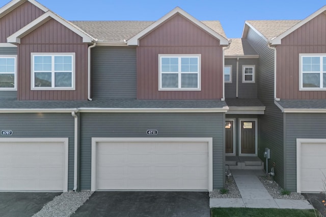 multi unit property with a garage, driveway, board and batten siding, and roof with shingles