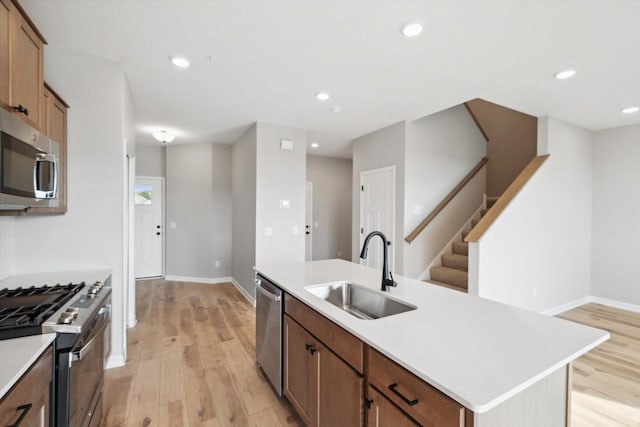 kitchen with a sink, light countertops, appliances with stainless steel finishes, brown cabinets, and a center island with sink