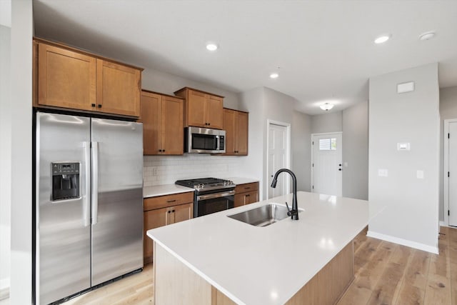 kitchen with appliances with stainless steel finishes, light countertops, a kitchen island with sink, and a sink