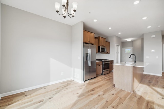 kitchen with a center island with sink, light wood-style flooring, decorative light fixtures, stainless steel appliances, and light countertops