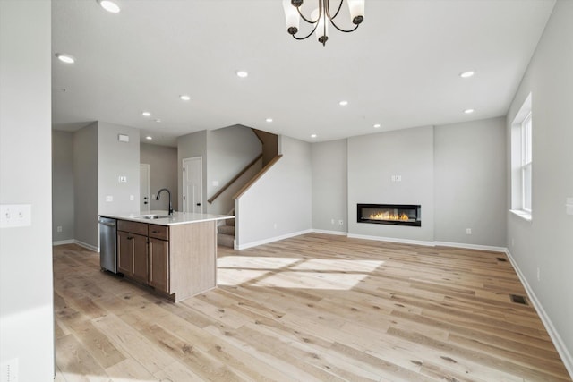 kitchen with a kitchen island with sink, a sink, open floor plan, light countertops, and a glass covered fireplace