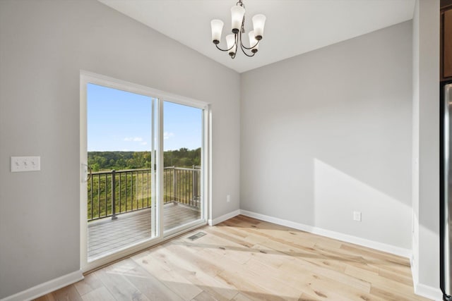 unfurnished room featuring baseboards, light wood finished floors, visible vents, and an inviting chandelier