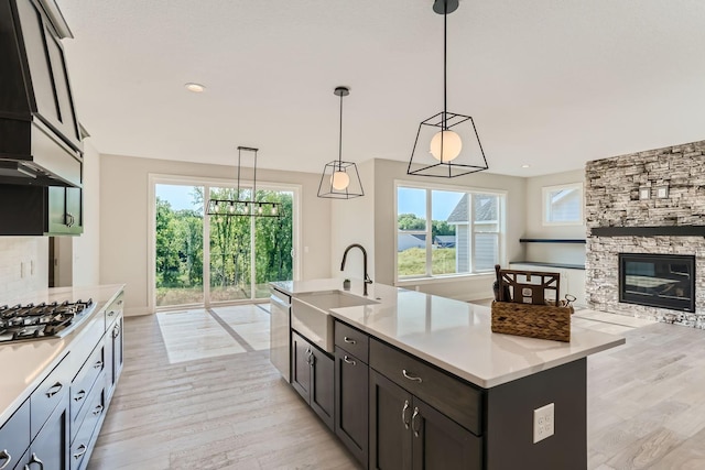 kitchen with a stone fireplace, a sink, open floor plan, hanging light fixtures, and a center island with sink