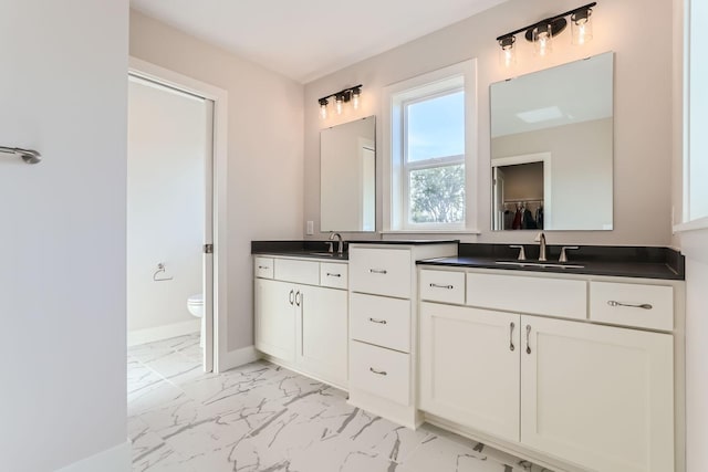 bathroom featuring marble finish floor, double vanity, a sink, and toilet