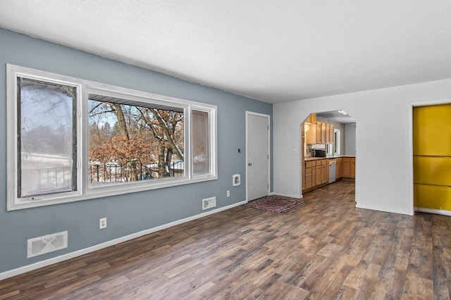 unfurnished living room featuring arched walkways, a textured ceiling, dark wood-type flooring, visible vents, and baseboards