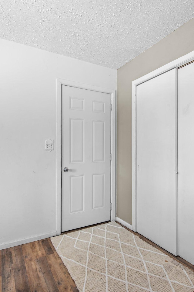 unfurnished bedroom featuring a closet, a textured ceiling, baseboards, and wood finished floors