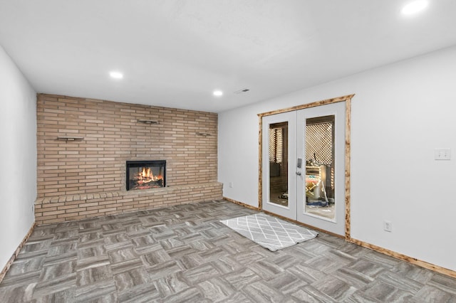 unfurnished living room featuring baseboards, brick wall, french doors, a fireplace, and recessed lighting