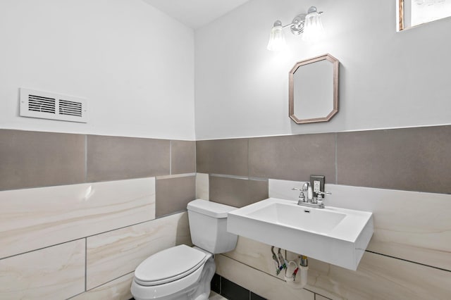 half bathroom with toilet, a wainscoted wall, a sink, visible vents, and tile walls