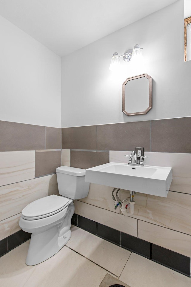 bathroom featuring tile patterned flooring, toilet, a wainscoted wall, a sink, and tile walls