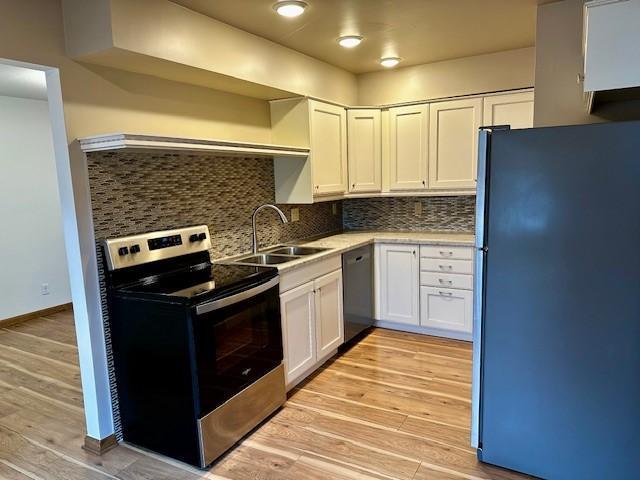 kitchen with light countertops, appliances with stainless steel finishes, white cabinetry, a sink, and light wood-type flooring