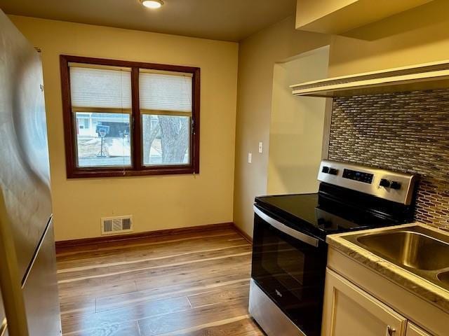 kitchen featuring visible vents, baseboards, light wood-style floors, freestanding refrigerator, and stainless steel electric range oven