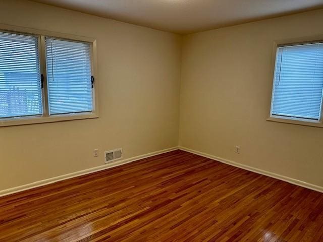 unfurnished room featuring baseboards, visible vents, and wood finished floors