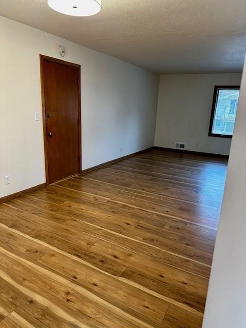 unfurnished room with a textured ceiling, wood finished floors, visible vents, and baseboards