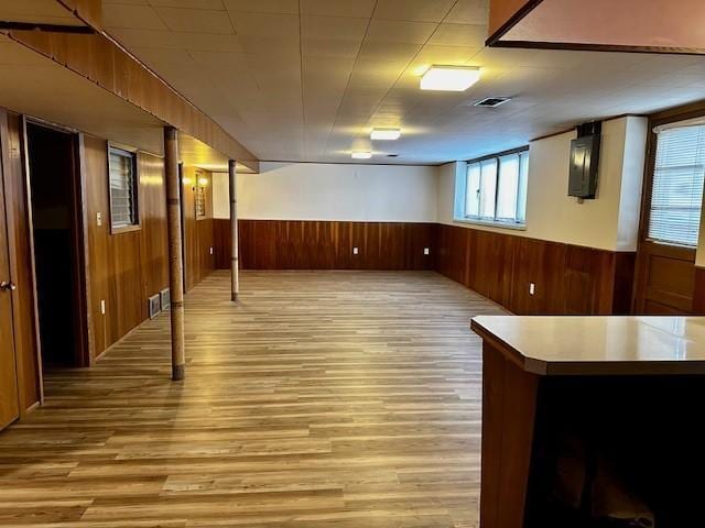 below grade area featuring light wood-type flooring, wood walls, visible vents, and wainscoting