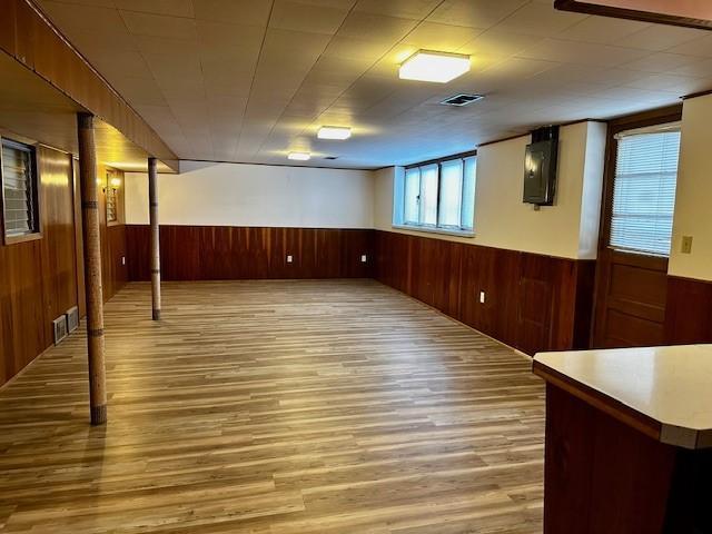 below grade area featuring a wainscoted wall, light wood-type flooring, visible vents, and wooden walls