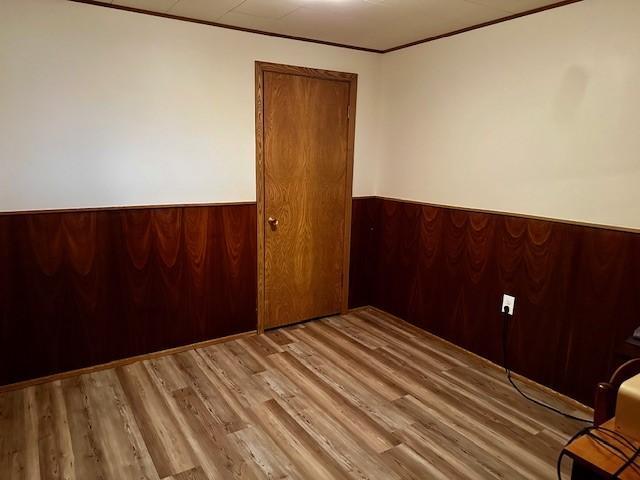 spare room featuring a wainscoted wall, crown molding, wood finished floors, and wooden walls