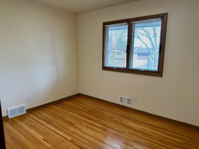 spare room with light wood-type flooring, visible vents, and baseboards