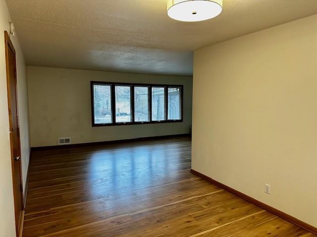 unfurnished room with baseboards, visible vents, dark wood finished floors, and a textured ceiling